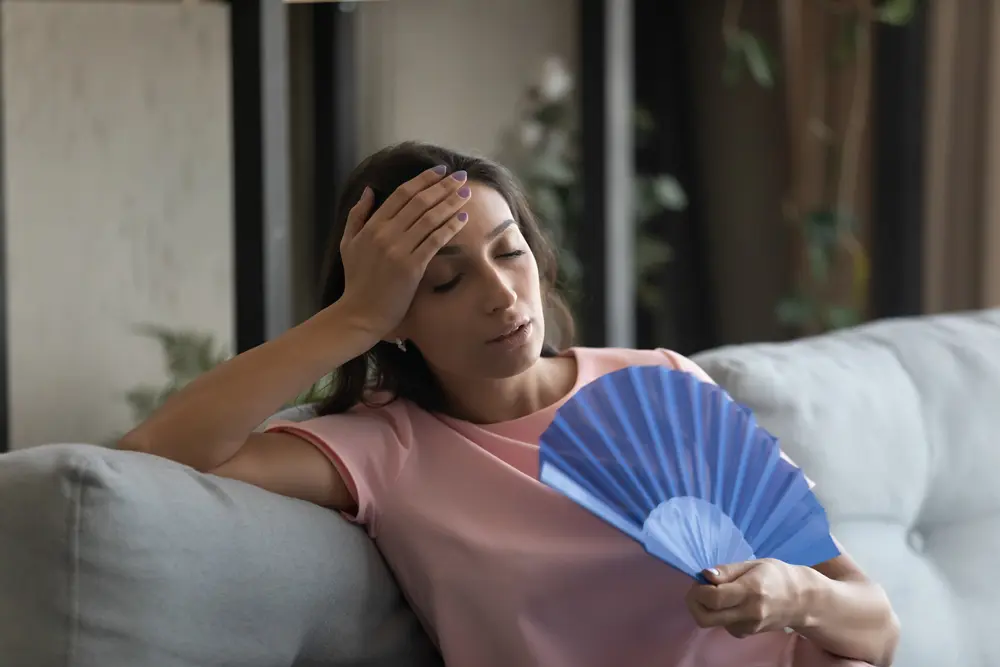 Too hot. Exhausted female suffer from high humidity in modern apartment use hand fan feel lack of air conditioning. Unhappy young mixed race female